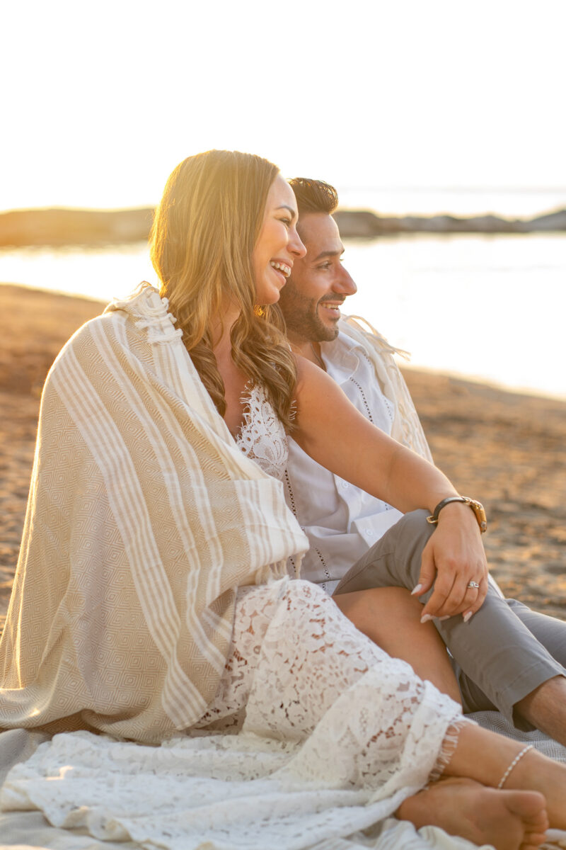Engaged couple smile while sitting on beach in Cleveland